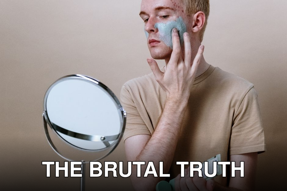 Young man applying clay mask for skincare routine indoors with a mirror.