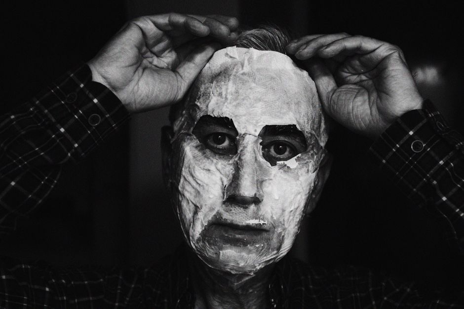 Moody black and white portrait of a man adjusting a facial mask.