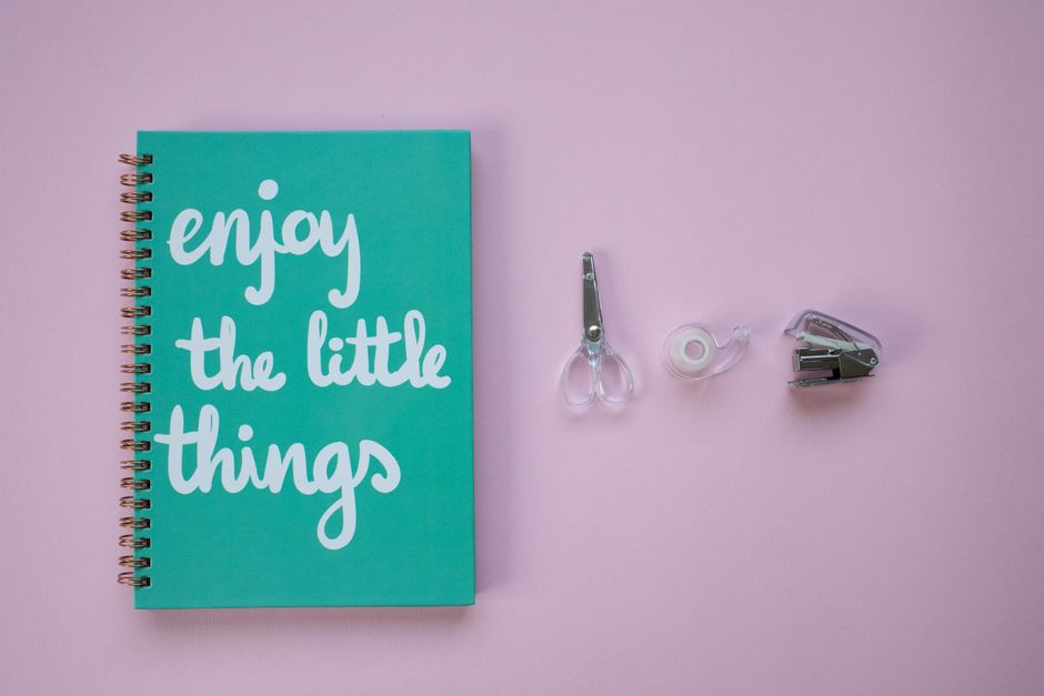 A pastel pink flat lay featuring a notebook with a motivational quote and office supplies.