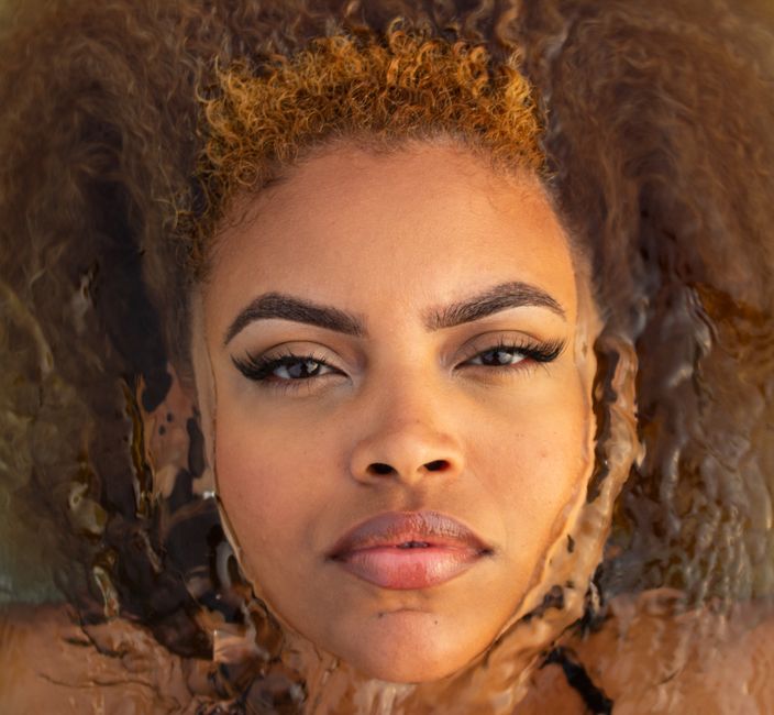 Serene close-up portrait of a woman with natural curly hair partially submerged in water.