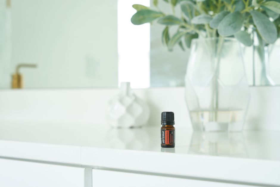 A close-up shot of an essential oil bottle on a white table with plants in the background, offering a clean and calming aesthetic.