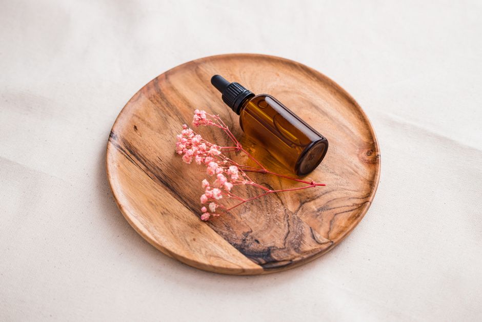 Brown glass dropper bottle with pink flowers on a wooden plate for skincare themes.