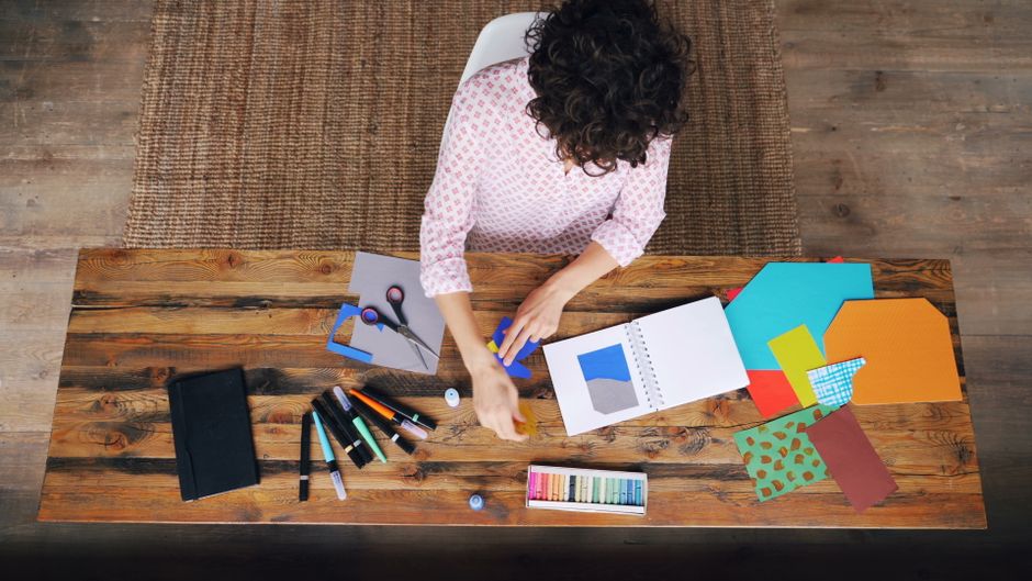 Overhead view of an adult woman doing arts and crafts at a wooden table.