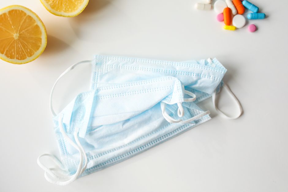 A flat lay of face masks, lemons, and pills on a white surface, emphasizing health and protection.