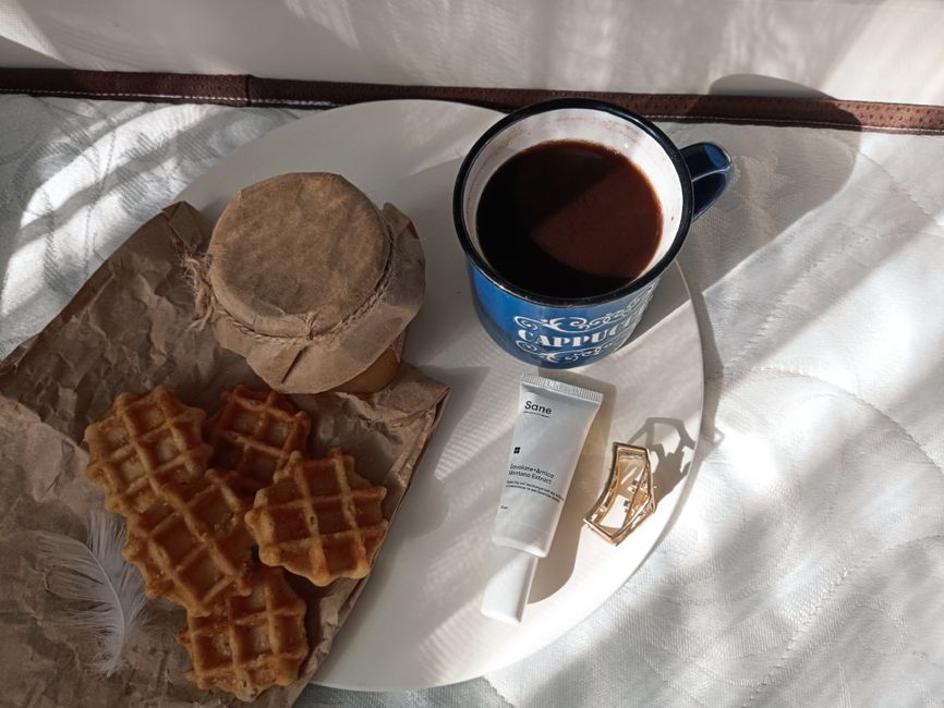 Flat lay of waffles, coffee, and personal items in a cozy morning setting.
