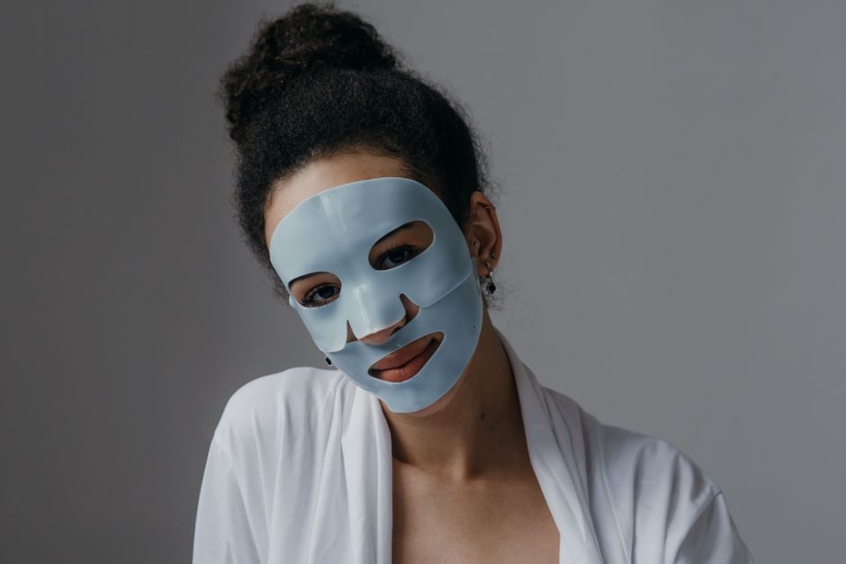 Adult woman enjoying a skincare routine with a blue sheet mask indoors.