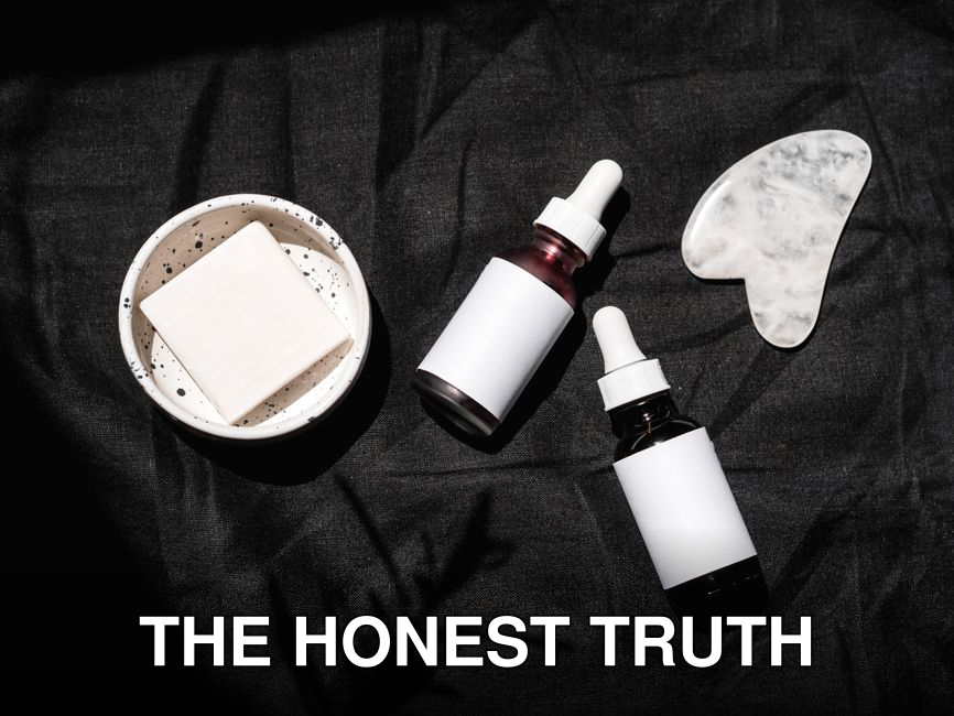 High-angle view of skincare products including serums, gua sha, and bar soap on a dark fabric backdrop.