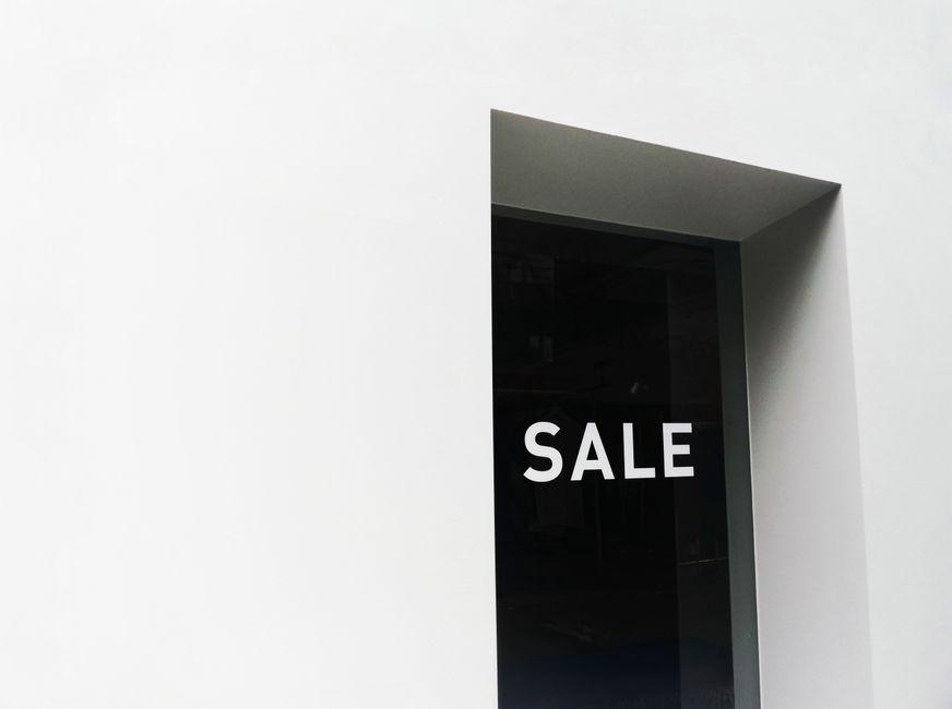 A minimalist black and white image of a sale sign on a store window with ample negative space.