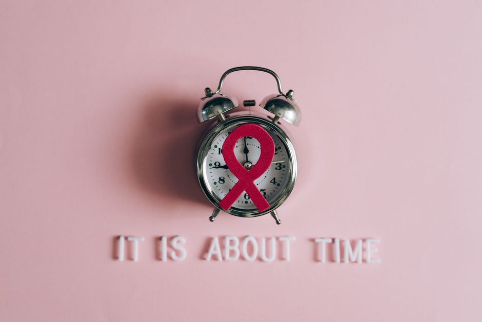 Alarm clock featuring an AIDS awareness ribbon on a pink background, symbolizing urgency and awareness.