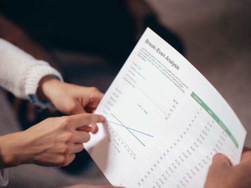 Close-up of hands discussing a break-even analysis document in a business meeting.