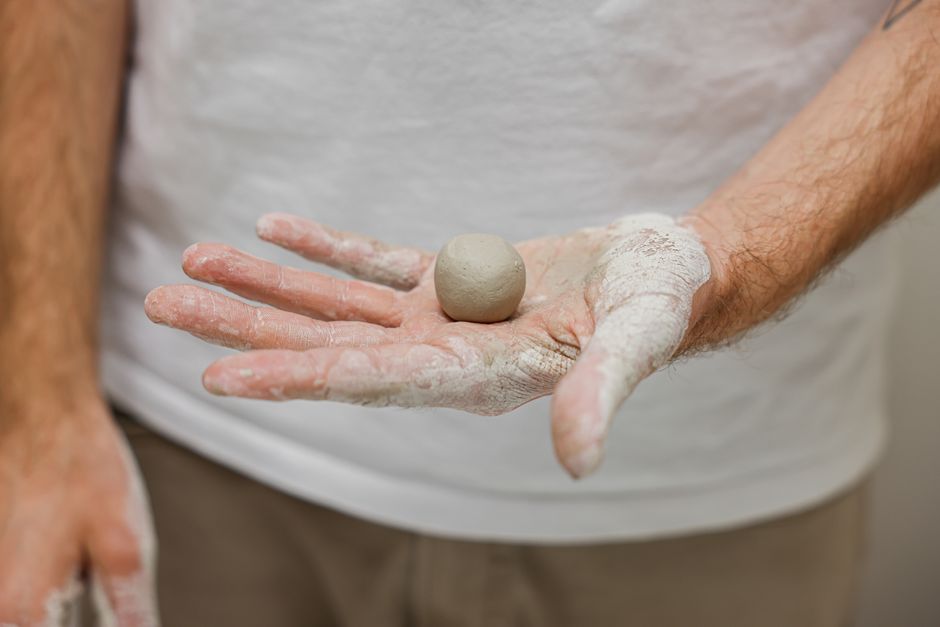 Close-up of artisan holding a small clay ball, showcasing the creative process of pottery making.
