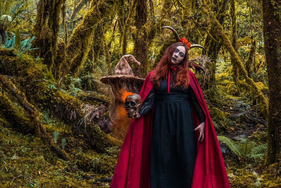 Witch in a vibrant forest holding a skull captures a spooky and enigmatic atmosphere.