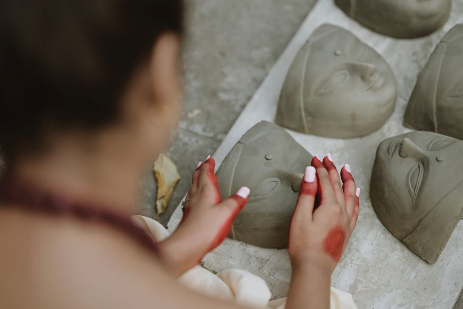 Artist with red-stained hands crafting traditional clay masks for festivals.