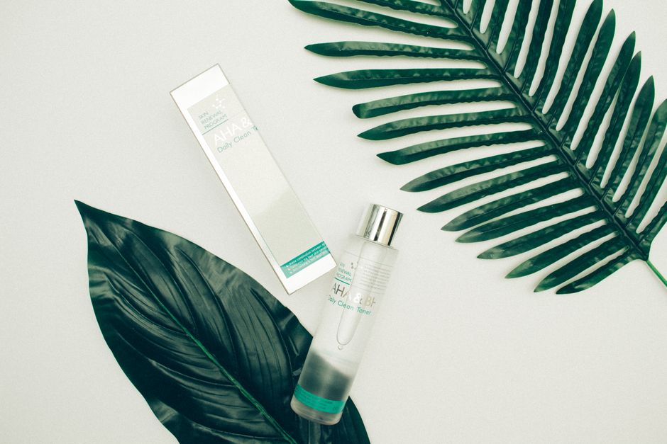 Top view composition of cosmetic products placed on white desk near fresh tropical green leaves