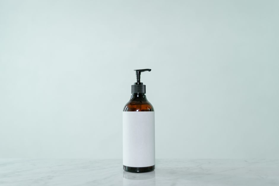 Minimalist display of a brown glass pump bottle with blank label on a light surface.