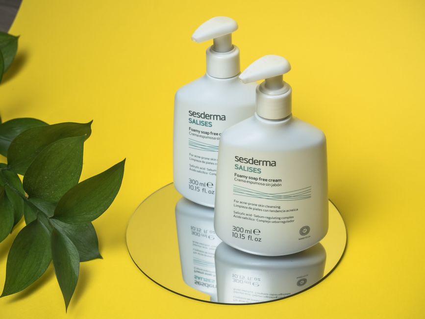 Sesderma Salises skin cream on mirror with yellow background, showcasing soothing skincare routine.