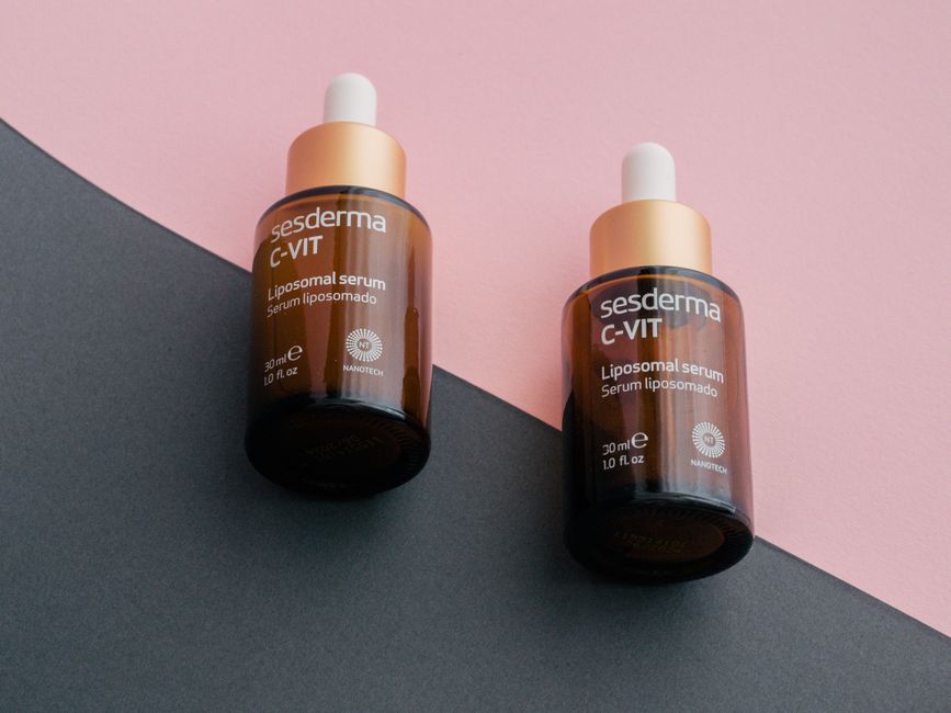 Two dropper bottles of Sesderma C-Vit liposomal serum on a pink and gray background.