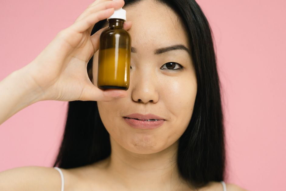 Young woman holding a brown cosmetic bottle against a pink background, showcasing beauty and skincare.