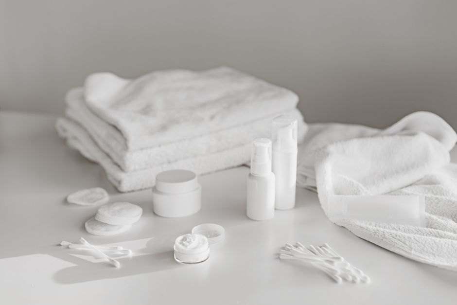 A neat arrangement of white skincare products and towels on a clean surface, perfect for spa and beauty themes.