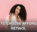 A woman with curly hair in a white robe examines two cosmetic oil bottles against a pink background.