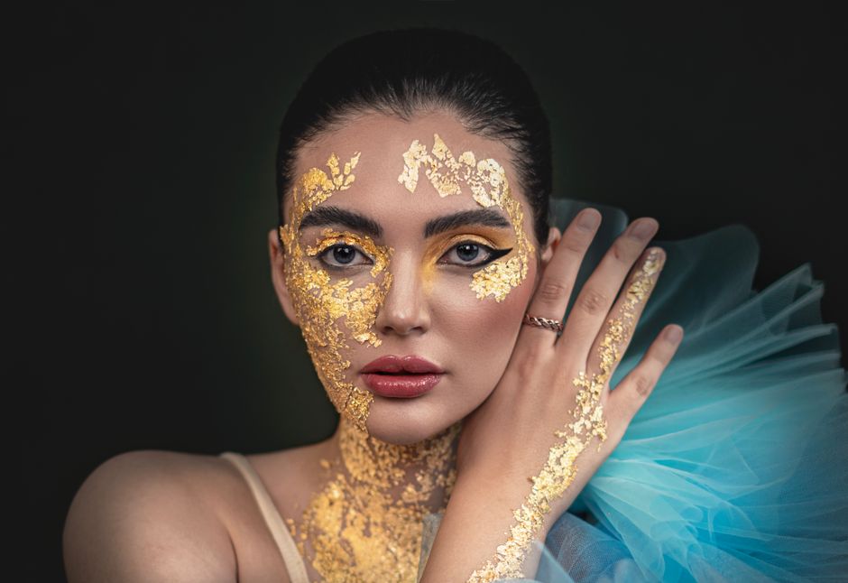 Portrait of a woman with stunning gold leaf art on her face and bold makeup.