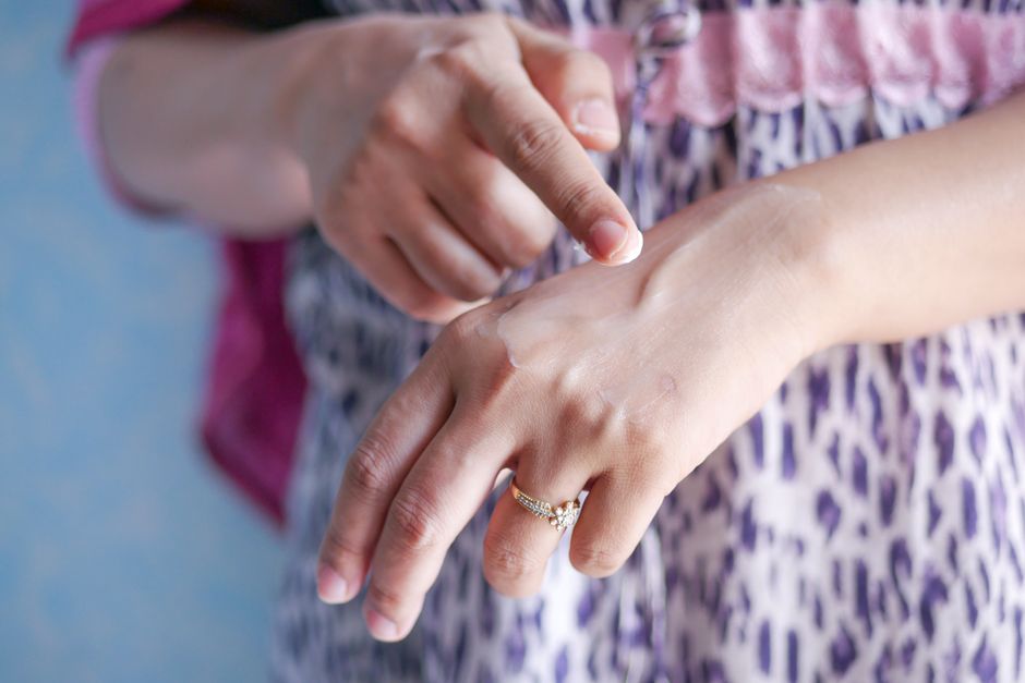 A woman applies skincare cream on her hand, highlighting moisturizing routine.