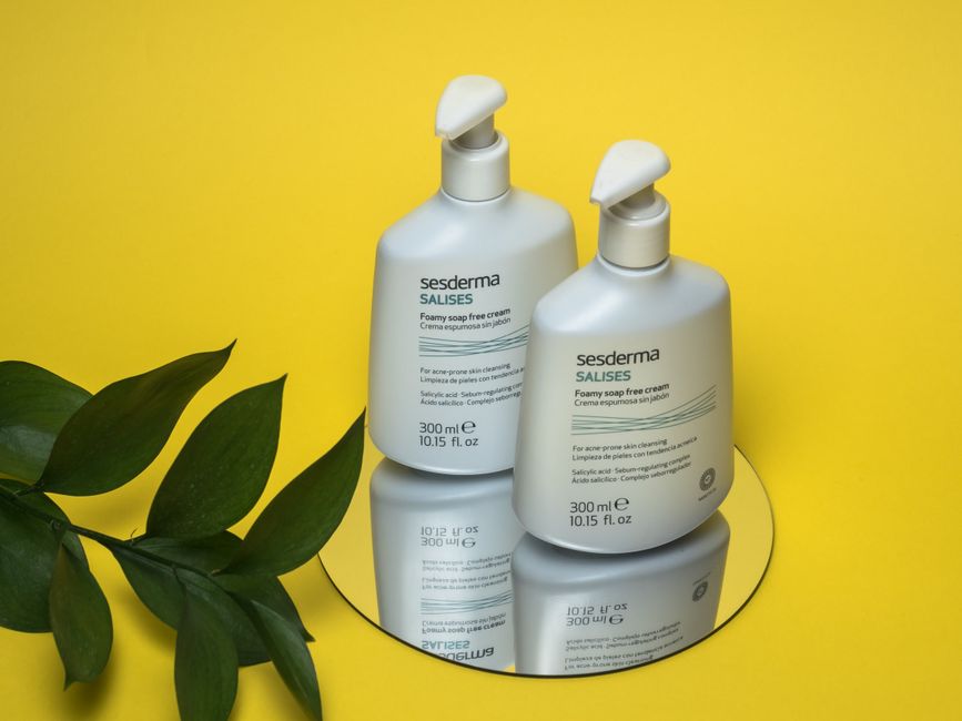 Minimalist skincare product bottles on a mirror with leaves on a yellow backdrop.