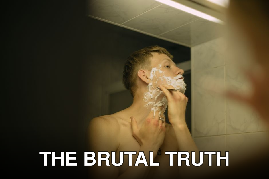 Adult man applying shaving cream while looking in bathroom mirror.