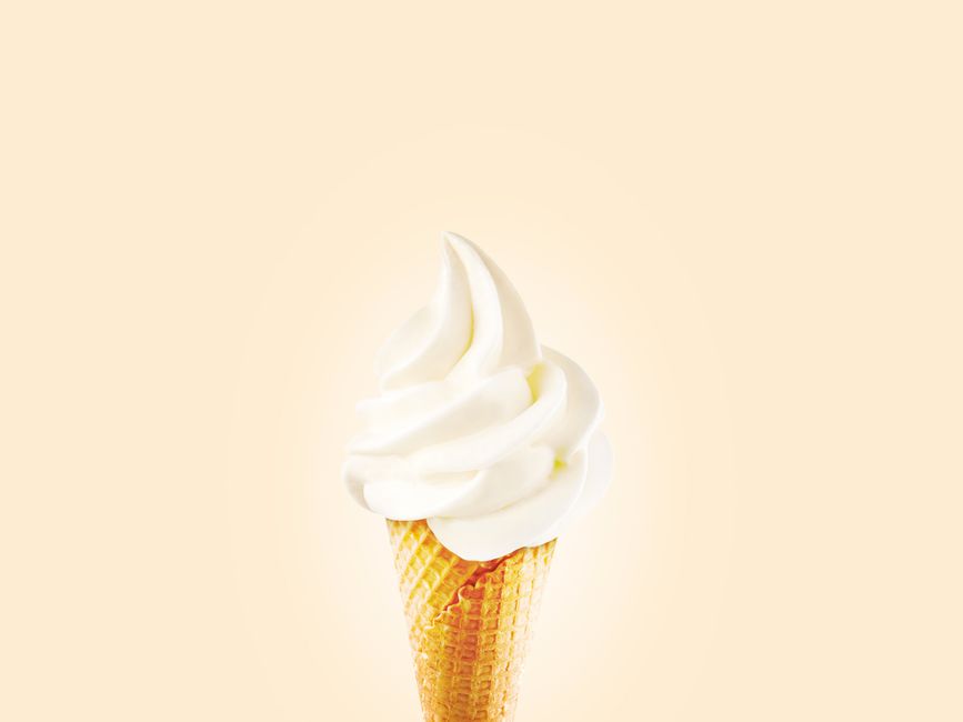 Close-up of a creamy soft serve ice cream cone on a bright background.