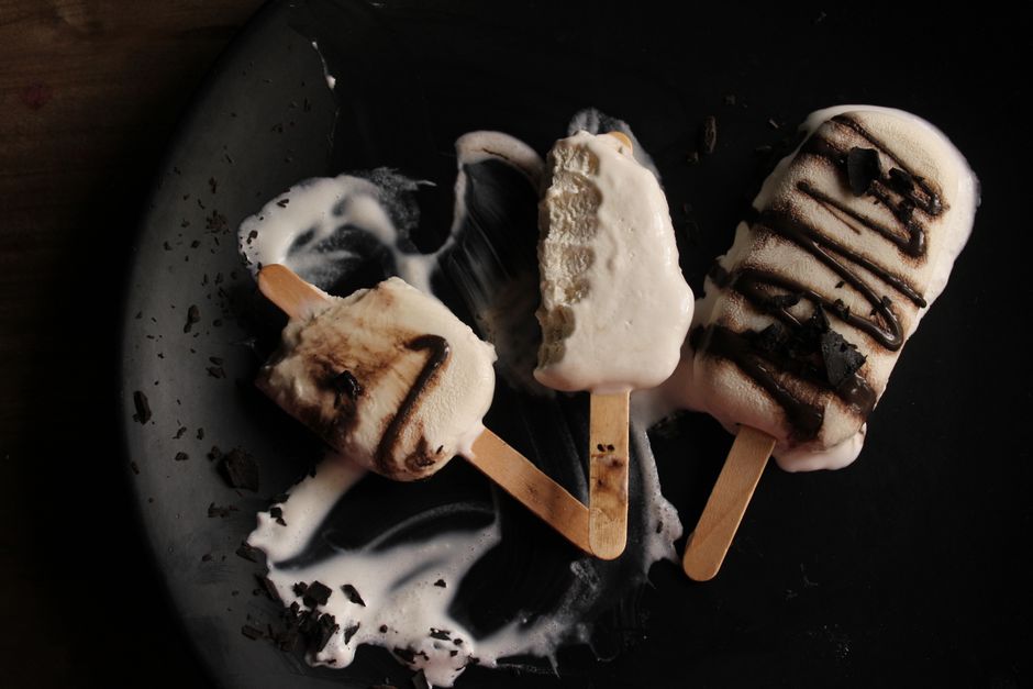 Three melted chocolate ice cream bars on a dark plate, artistically arranged.