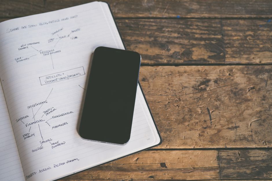 Smartphone resting on a notebook with handwritten notes on a rustic wooden table, ideal for business planning concepts.