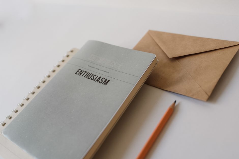 Close-up of a notepad with 'Enthusiasm' text, pencil, and envelope on white background.