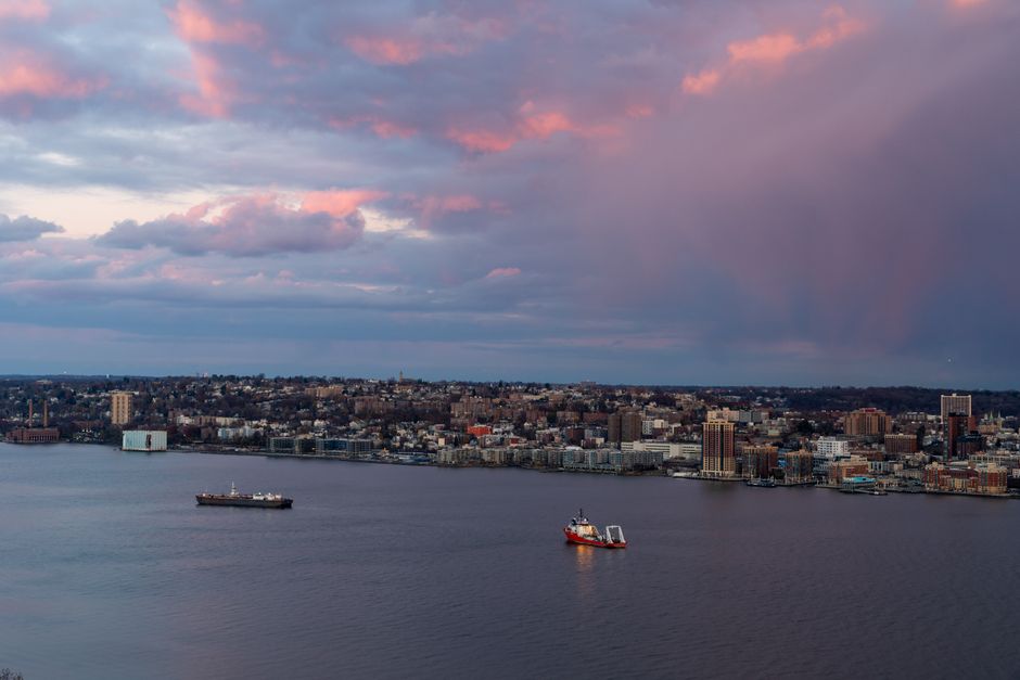 Vibrant sunrise over a cityscape with colorful clouds and ships on the water.