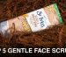 Close-up of a St Ives Gentle Smoothing Scrub tube surrounded by foliage.